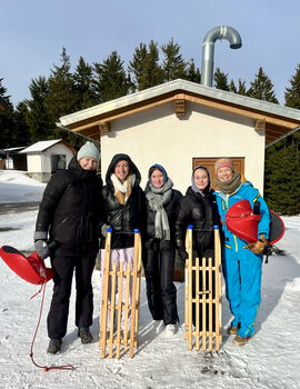 Fünf Schülerinnen mit Schlitten stehen vor einem Haus im Schnee