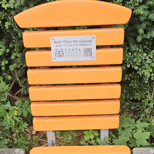 Eine Plakette mit der Aufschrift "Kein Platz für Gewalt gegen Frauen und Mädchen!" und dem Logo von ZONTA Club Erlangen an einer orangenen Bank
