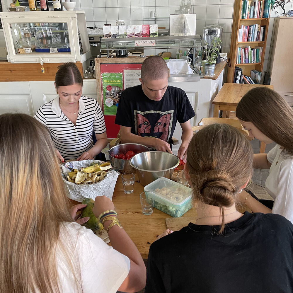 Eine Gruppe Jugendlicher beim Kochen gemeinsam an einem großen Tisch. Alle arbieten und schneiden Gemüse, in der Mitte einige Schüsseln